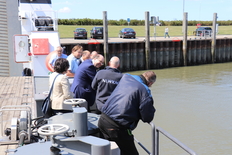 Umweltminister Christian Meyer und Mitarbeiter*innen des NLWKNs stehen auf einem Boot über die Reling gebeugt, rechts von ihnen sieht man Wasser