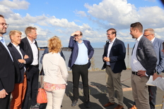 Minister Meyer und eine Gruppe an Terminbegleiter*innen stehen auf einer Straße, im Hintergrund sieht man Wasser