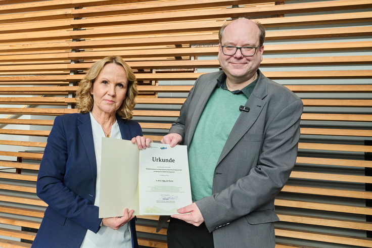 Minister Meyer bekommt von Bundesumweltministerin Steffi Lemke den Förderbescheid überreicht. Beide lachen in die Kamera.